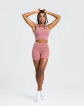 وصف: امرأة ترتدي قميصًا رياضيًا Essential Crop Tank Top بلون وردي فاتح من WOMEN'S BEST.